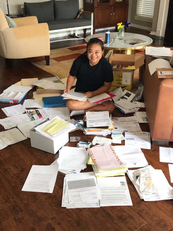 A picture of the owner, Julianna, sitting on a living room floor and surrounded by piles of papers all around her.